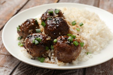 Photo of Delicious rice with meatballs, sauce and green onions on wooden table, closeup