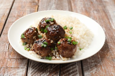 Photo of Delicious rice with meatballs, sauce and green onions on wooden table, closeup