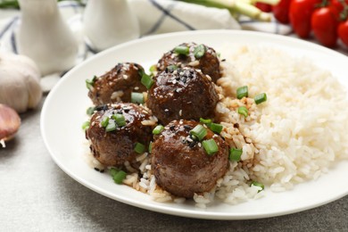 Photo of Delicious rice with meatballs, sauce and green onions on grey table, closeup