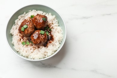 Photo of Delicious rice with meatballs, sauce and green onions in bowl on white marble table, top view. Space for text