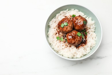 Photo of Delicious rice with meatballs, sauce and green onions in bowl on white marble table, top view. Space for text