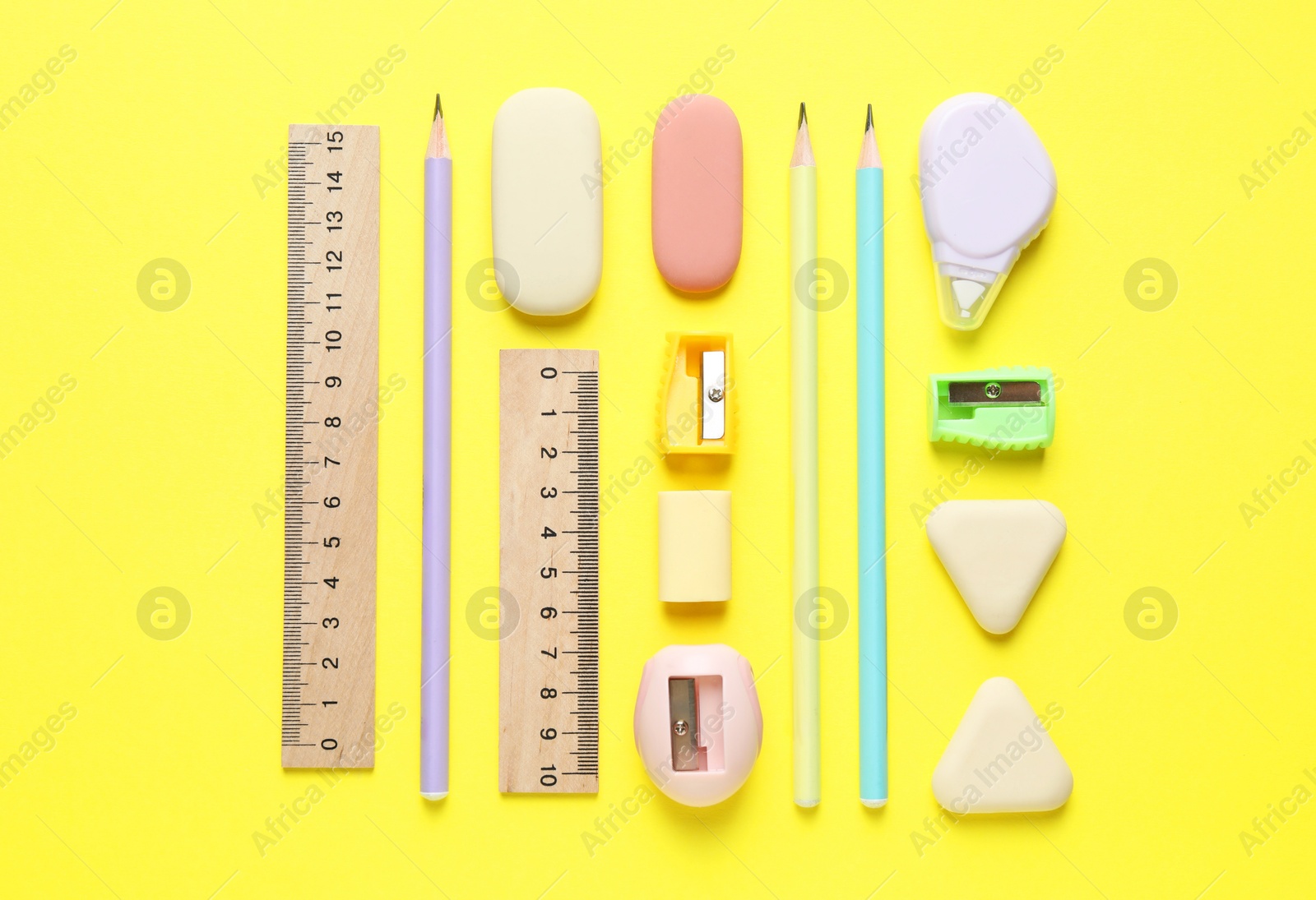 Photo of Erasers and other stationery on yellow background, flat lay