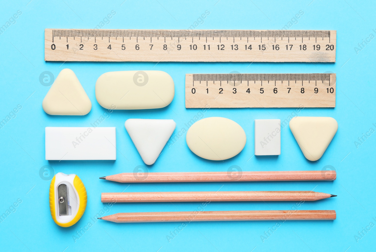 Photo of Erasers and other stationery on light blue background, flat lay