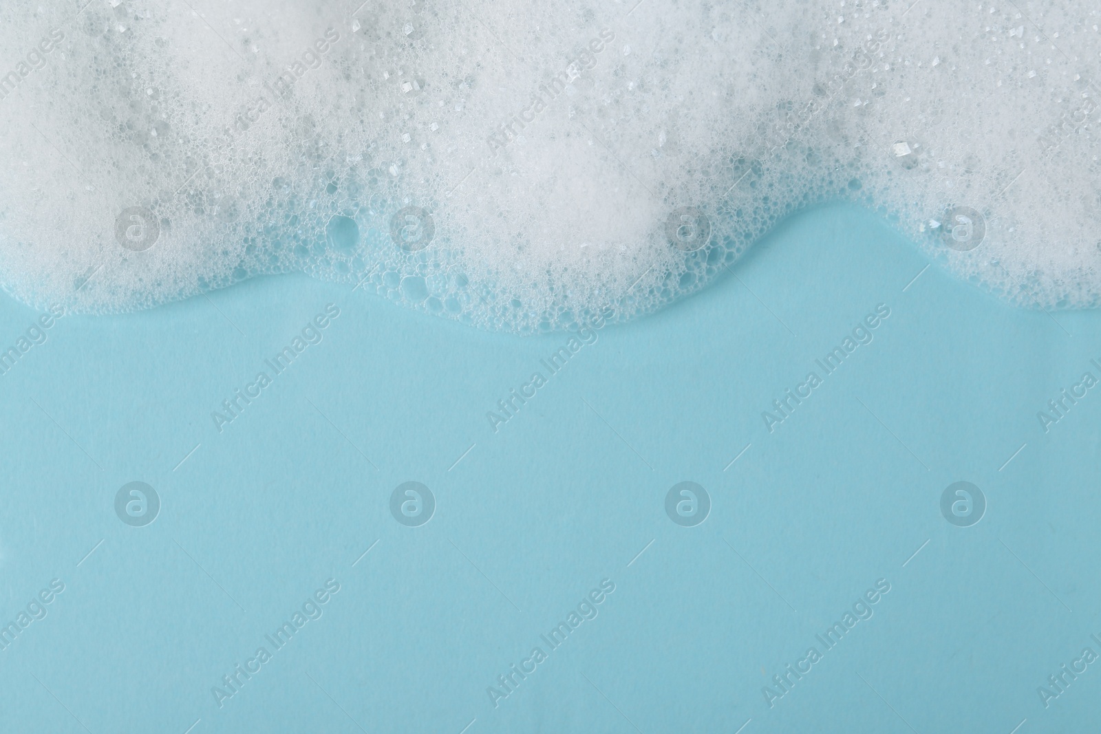 Photo of White fluffy foam on light blue background, top view. Space for text