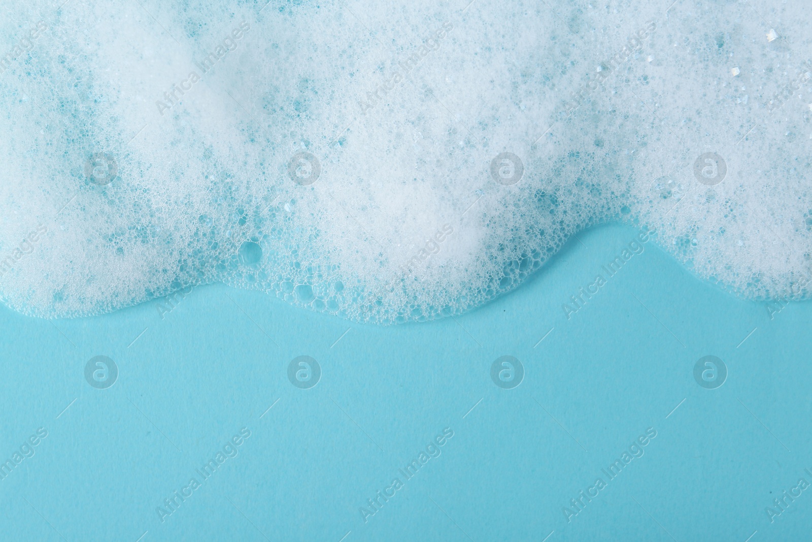 Photo of White fluffy foam on light blue background, top view. Space for text