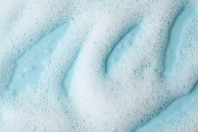 Photo of White fluffy foam on light blue background, top view