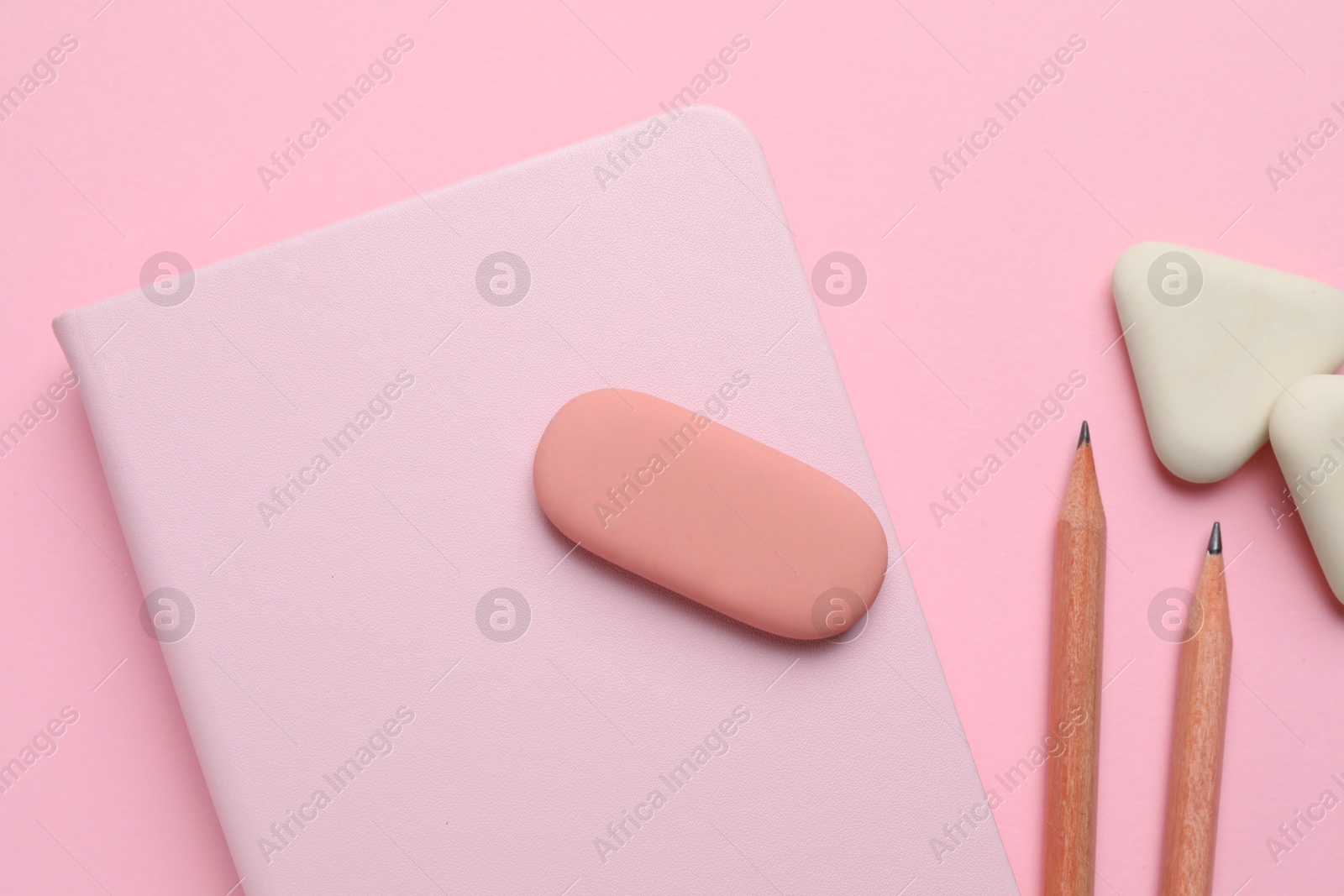 Photo of Erasers, notebook and pencils on pink background, flat lay