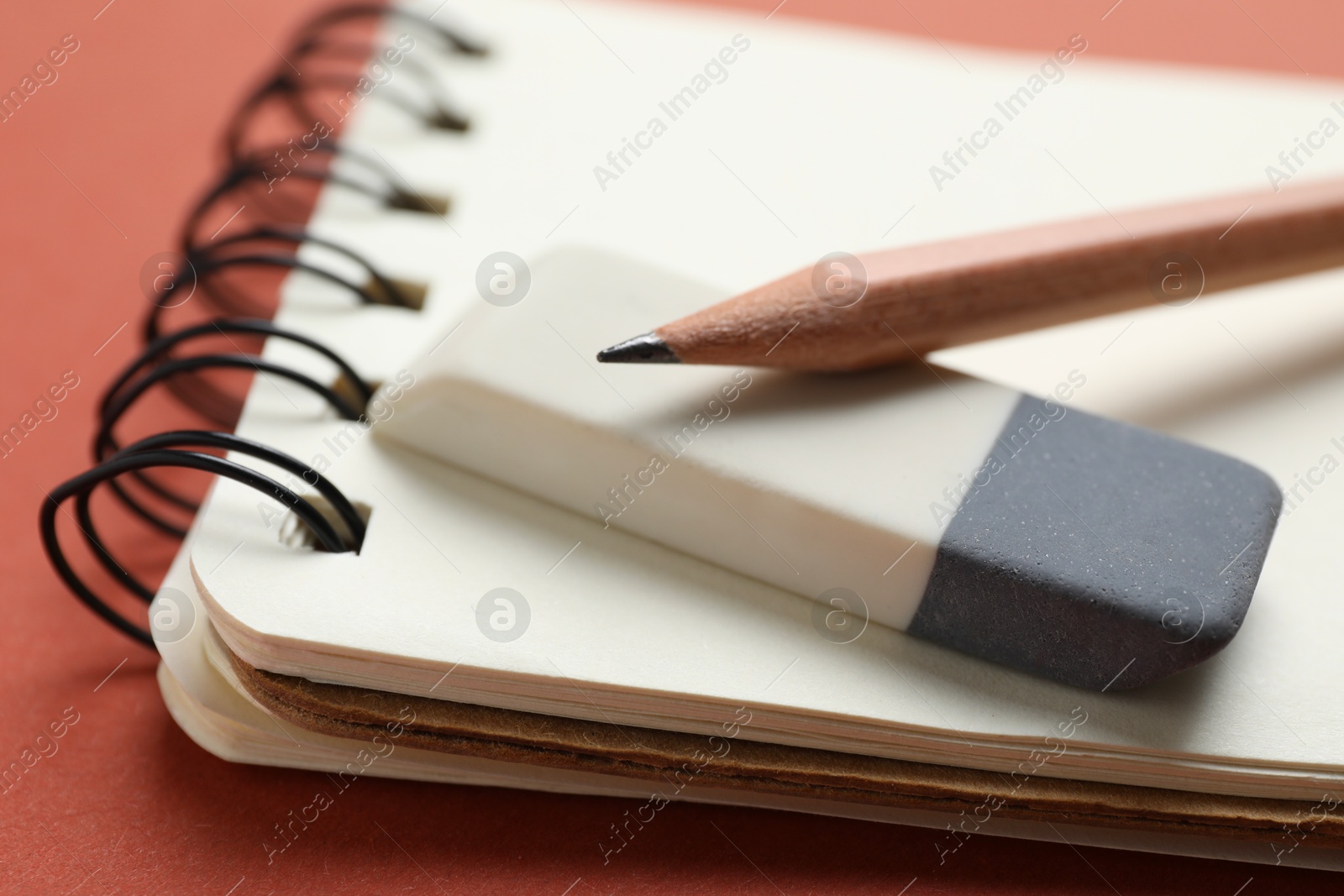 Photo of Eraser, pencils and notebook on brown background, closeup