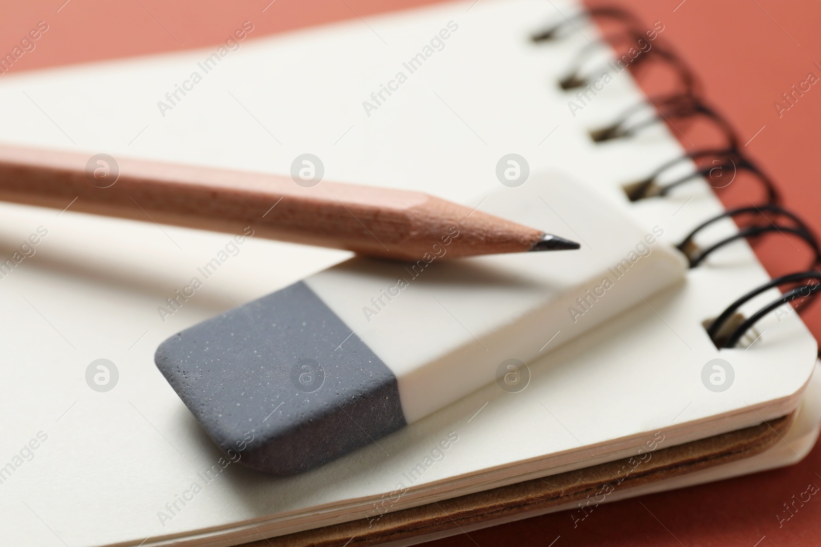 Photo of Eraser, pencils and notebook on brown background, closeup