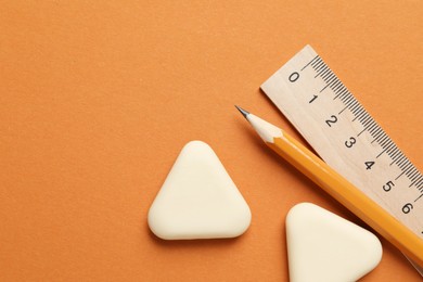 Photo of Erasers, ruler and pencil on orange background, flat lay. Space for text