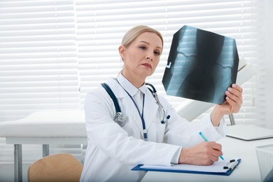 Photo of Doctor examining x-ray image of knee while working at table in clinic