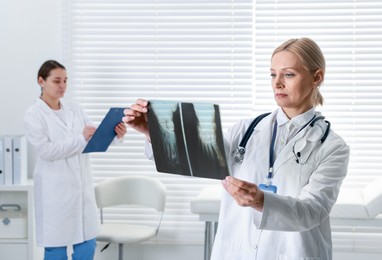 Photo of Doctor examining x-ray image of foot in clinic. Medical assistant with clipboard indoors