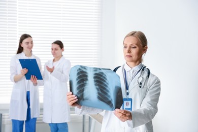 Photo of Doctor examining chest x-ray in clinic. Medical assistants with clipboard indoors