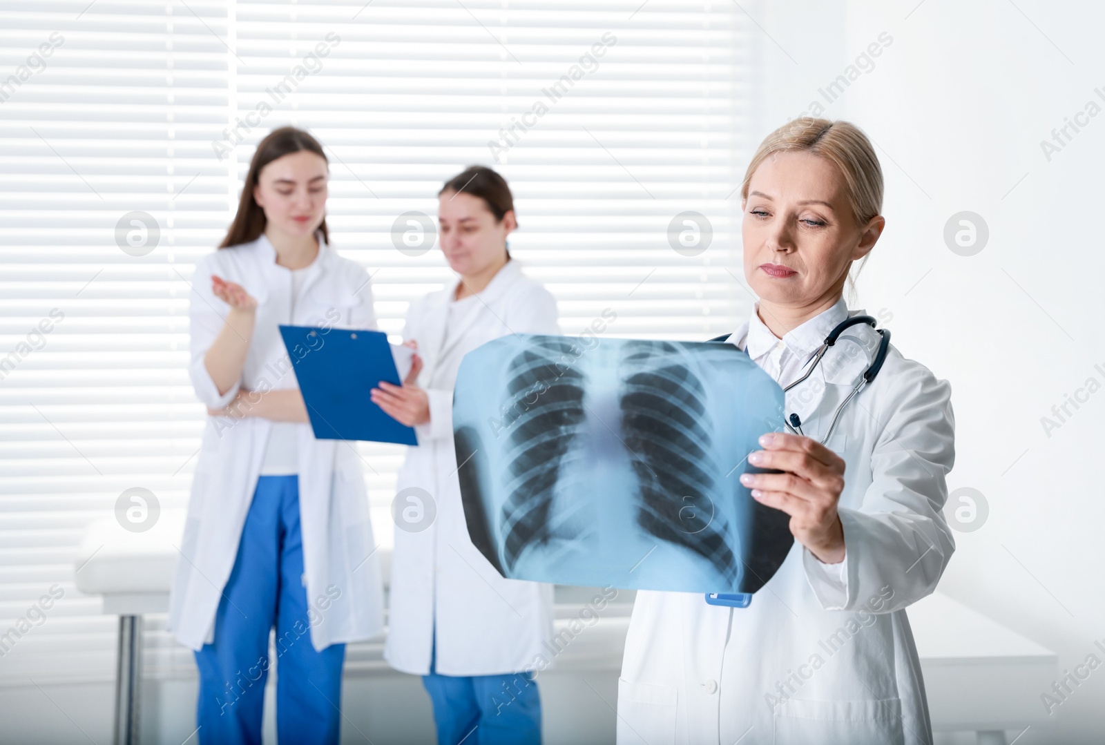 Photo of Doctor examining chest x-ray in clinic. Medical assistants with clipboard indoors