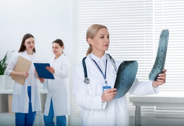 Photo of Doctor examining x-ray images of backbone in clinic. Medical assistants with clipboards indoors