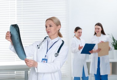 Photo of Doctor examining x-ray image of backbone in clinic. Medical assistants with clipboards indoors