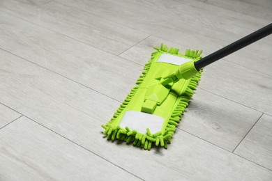 Microfiber mop on wooden floor, space for text