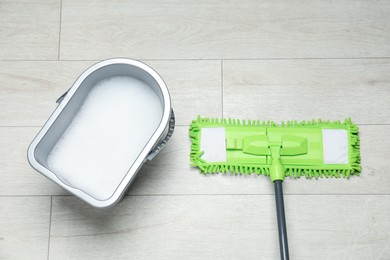 Photo of Microfiber mop and bucket with detergent on wooden floor, top view