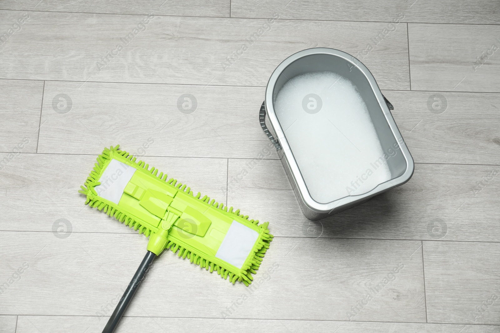 Photo of Microfiber mop and bucket with detergent on wooden floor, top view