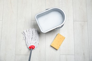 Photo of String mop, sponge and bucket with detergent on wooden floor, flat lay