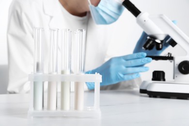 Photo of Laboratory testing. Scientist working with microscope at white marble table, focus on test tubes