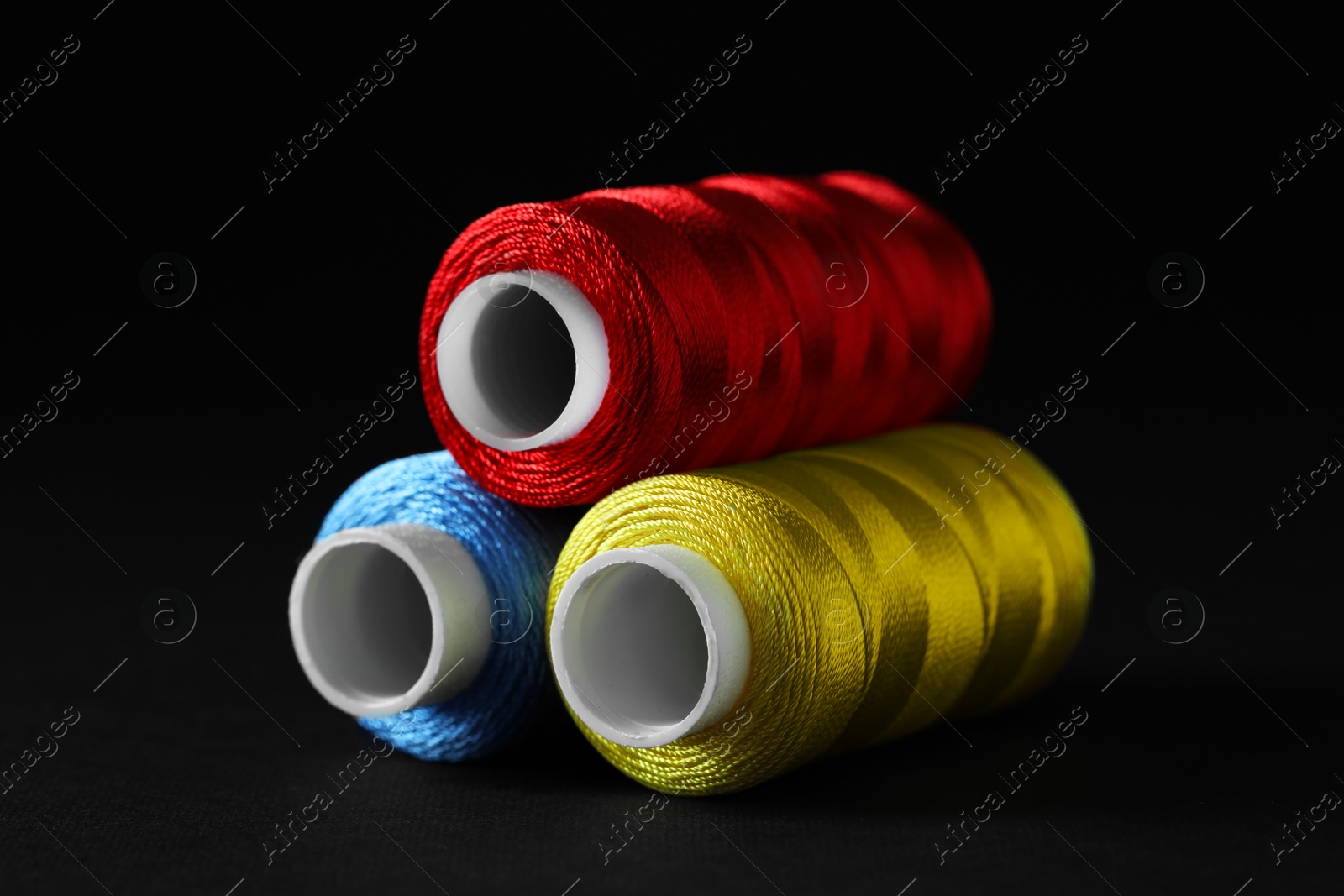 Photo of Spools of colorful sewing threads on black background, closeup