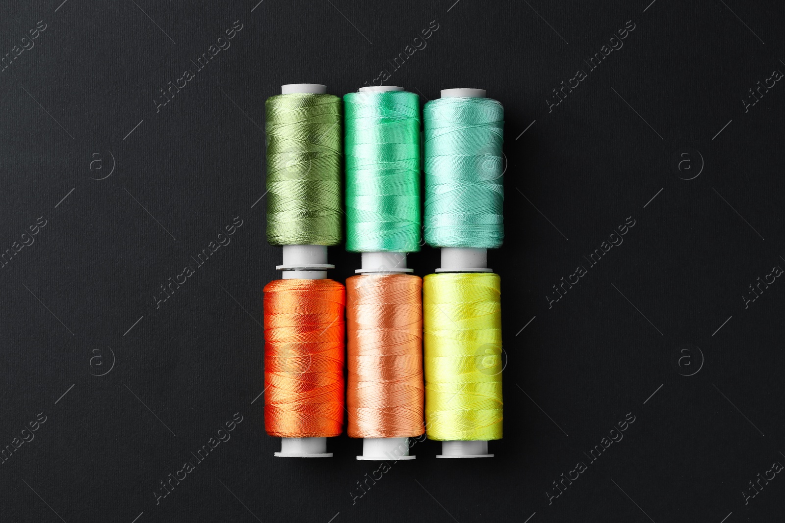 Photo of Spools of colorful sewing threads on black background, flat lay