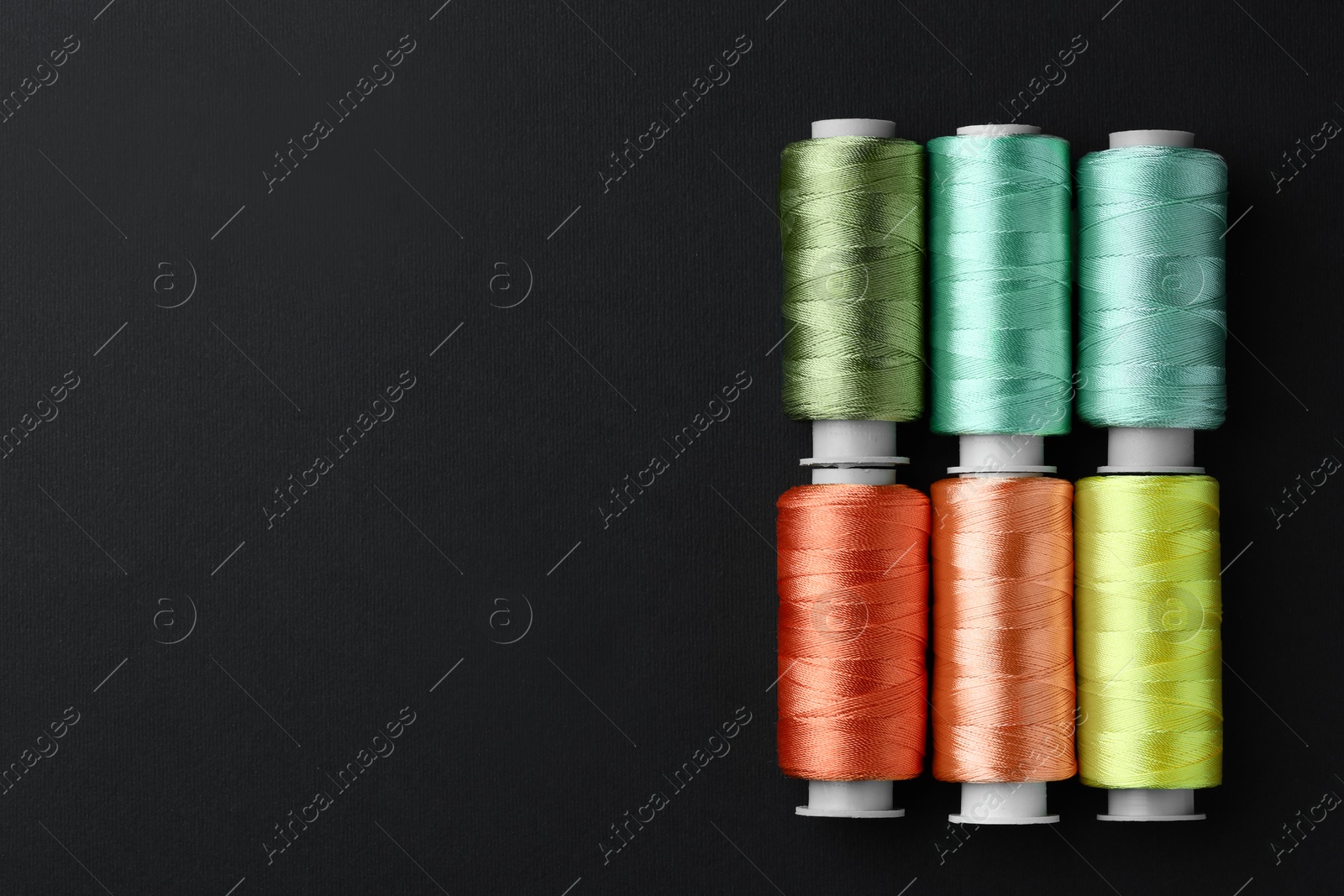 Photo of Spools of colorful sewing threads on black background, flat lay. Space for text