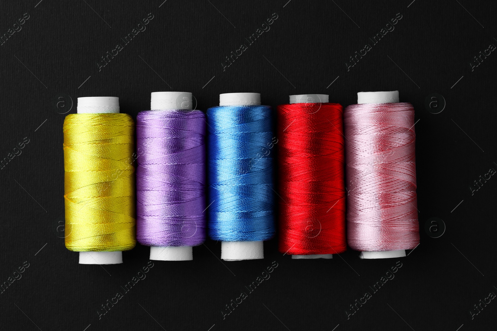 Photo of Spools of colorful sewing threads on black background, flat lay