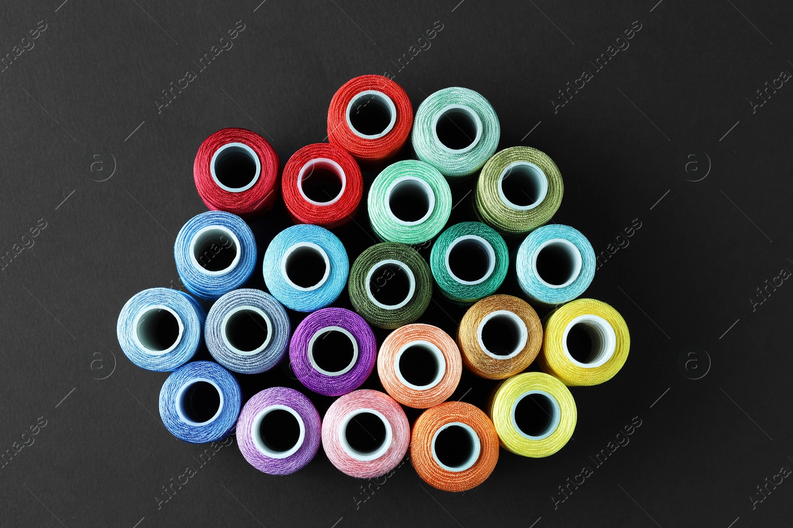 Photo of Spools of colorful sewing threads on black background, flat lay