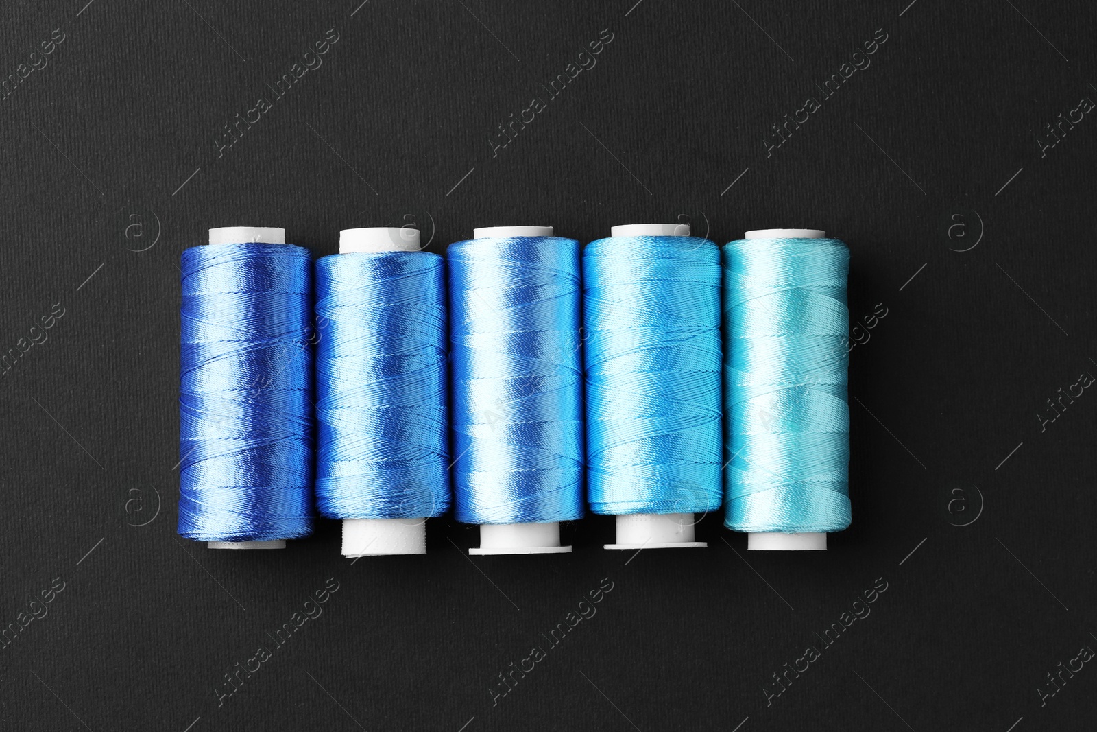 Photo of Spools of colorful sewing threads on black background, flat lay