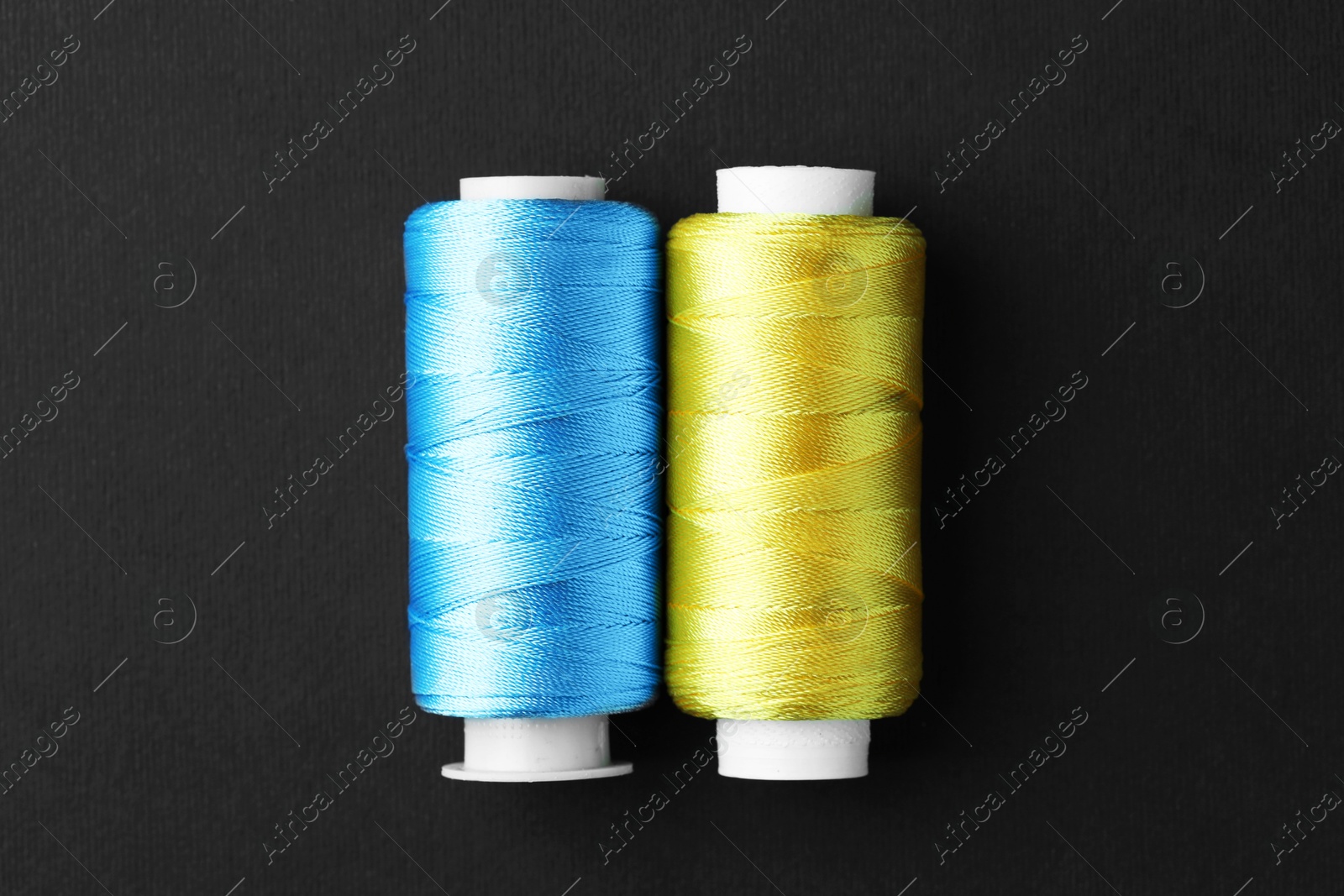 Photo of Spools of colorful sewing threads on black background, top view