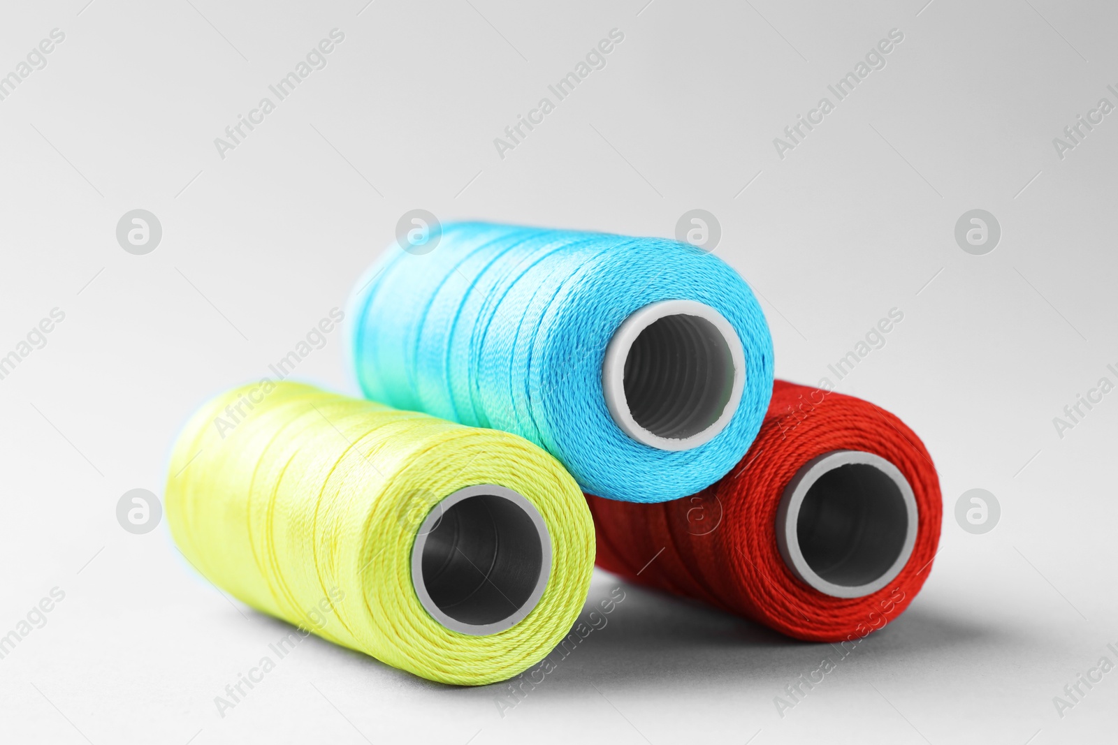 Photo of Spools of colorful sewing threads on light background, closeup