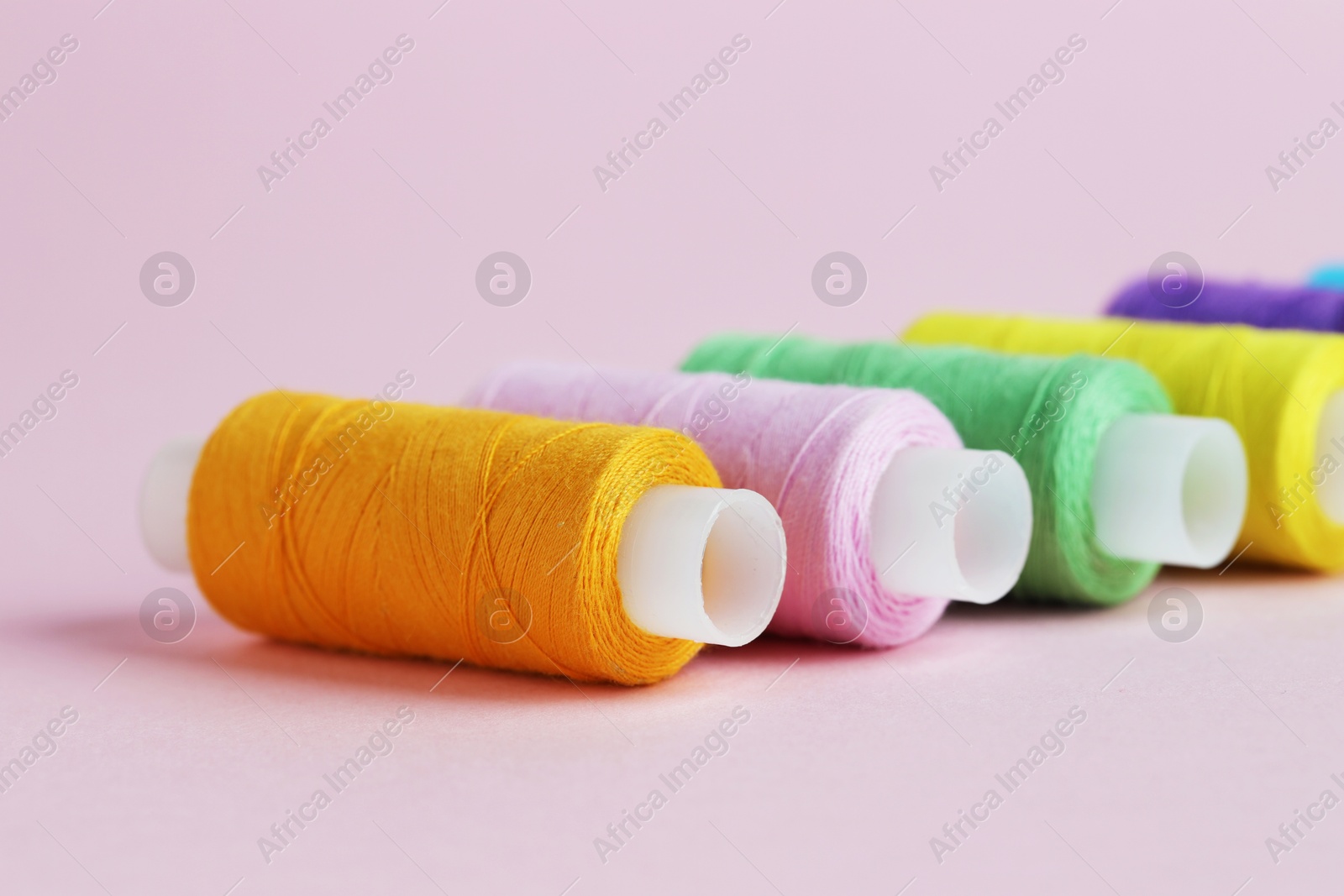 Photo of Spools of colorful sewing threads on pink background, closeup