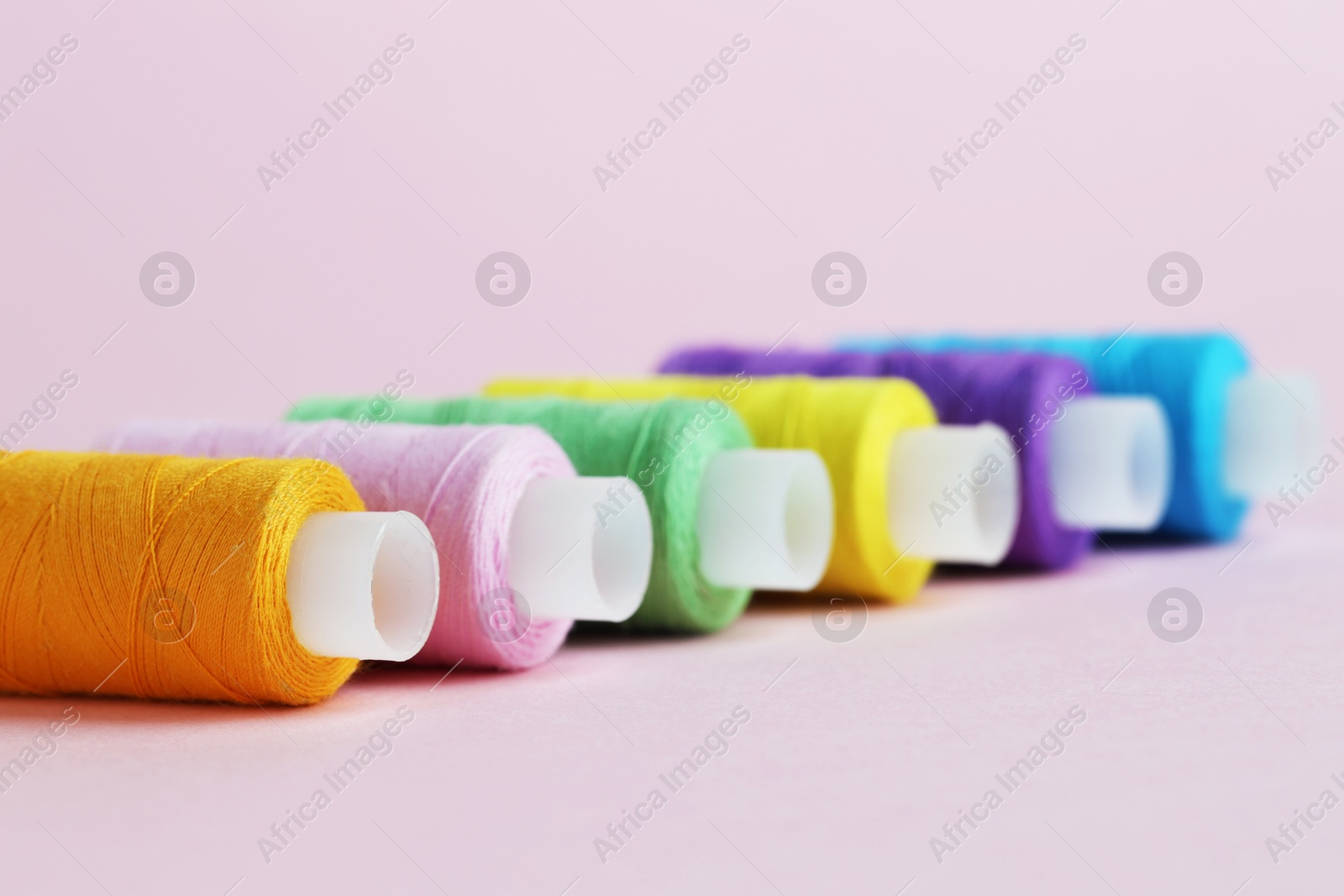 Photo of Spools of colorful sewing threads on pink background, closeup