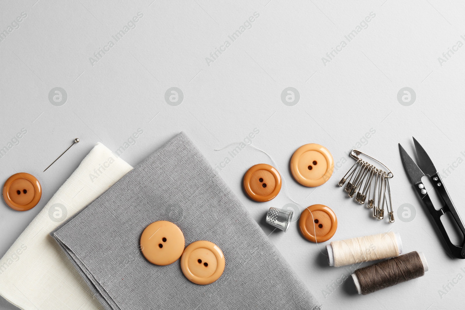 Photo of Different sewing supplies and fabric on light grey background, flat lay. Space for text