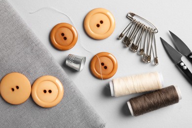 Photo of Different sewing supplies and fabric on light grey background, flat lay