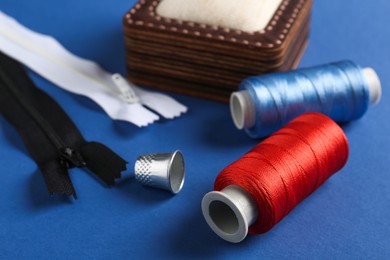 Photo of Different sewing supplies on blue background, closeup