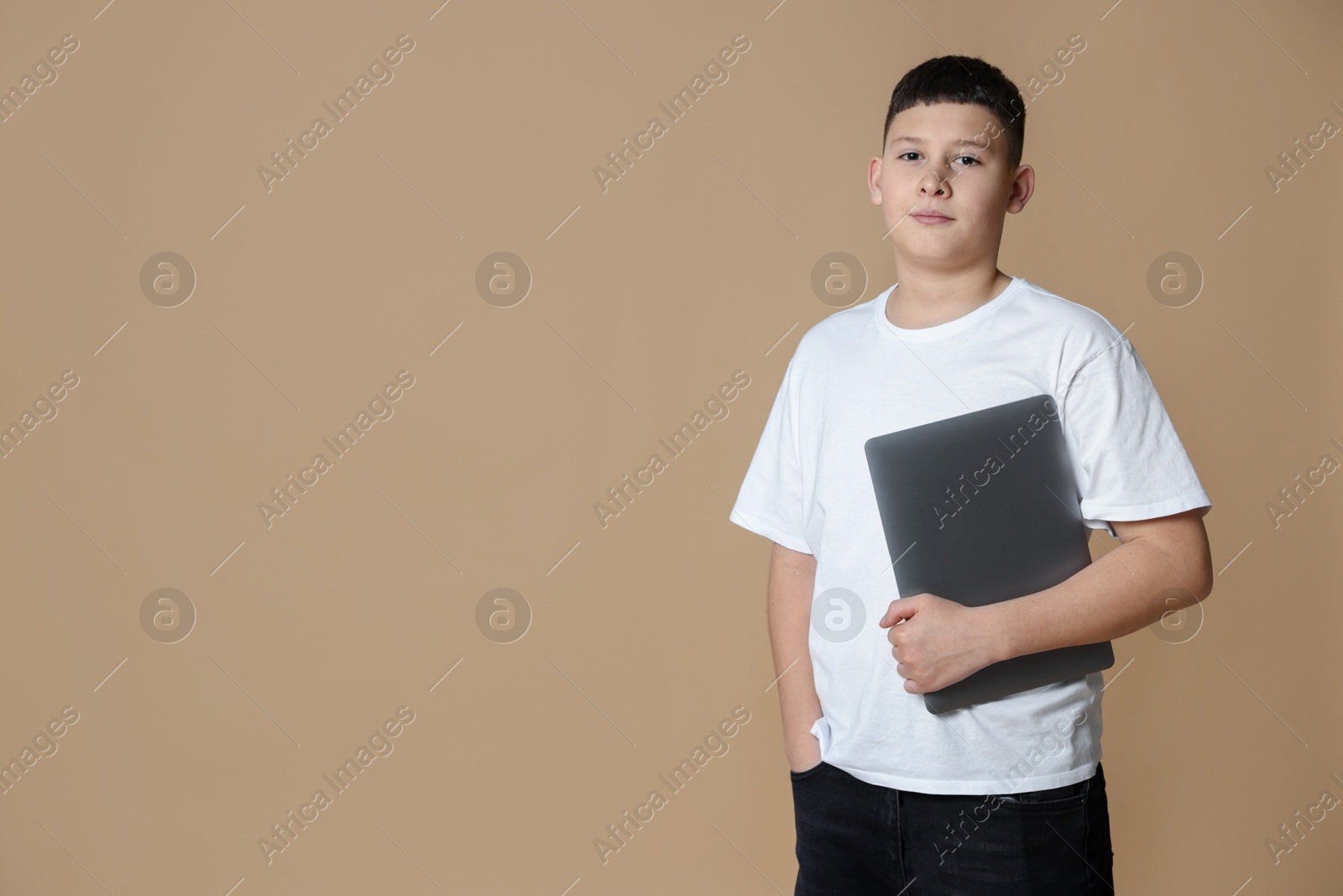 Photo of Portrait of teenage boy with laptop on beige background, space for text