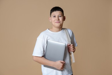 Photo of Portrait of teenage boy with laptop and backpack on beige background