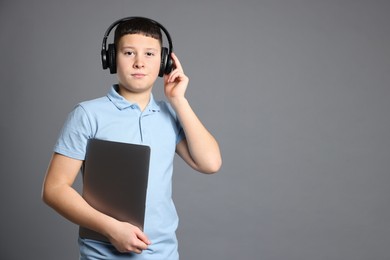 Photo of Portrait of teenage boy with laptop and headphones on grey background, space for text