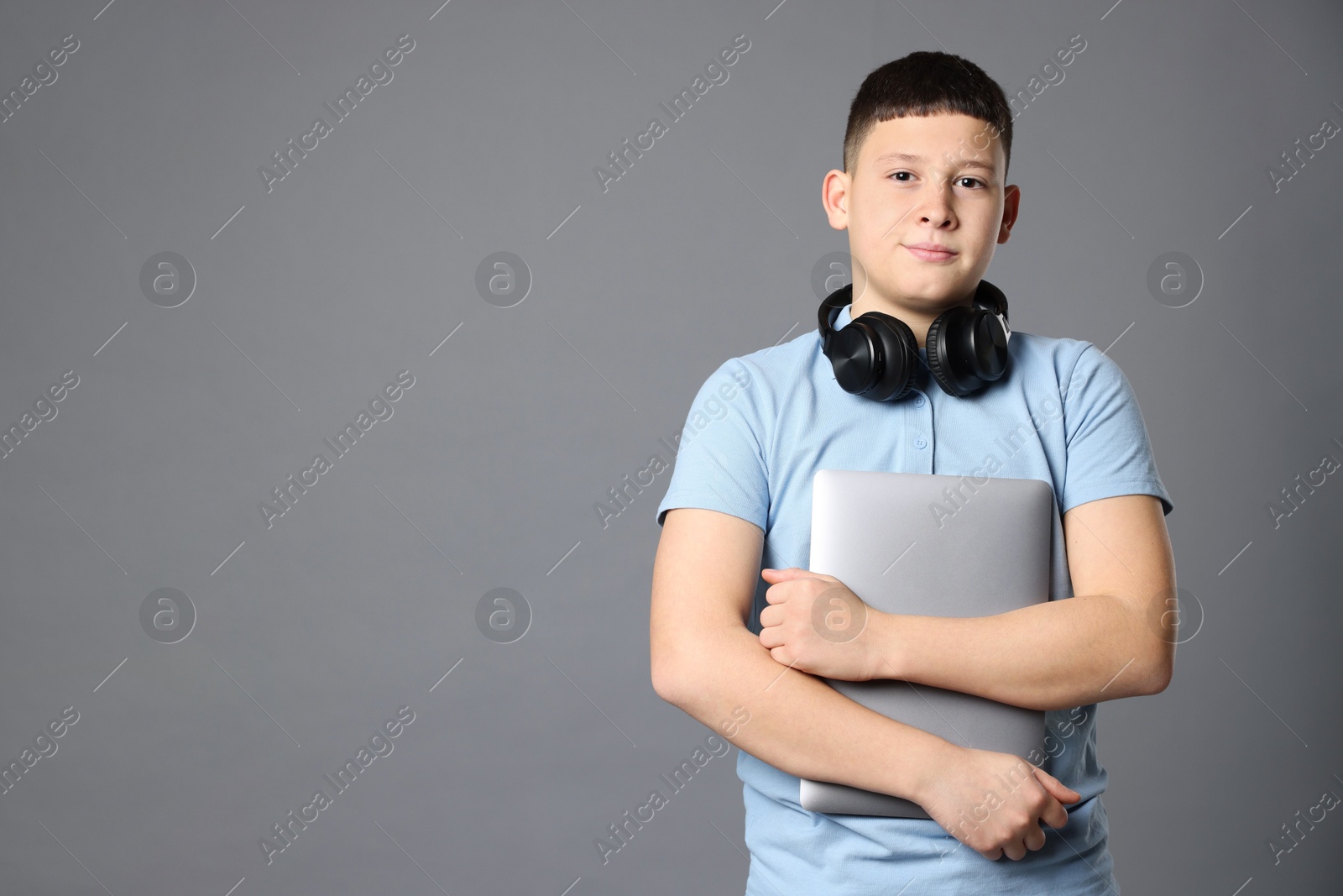 Photo of Portrait of teenage boy with laptop and headphones on grey background, space for text