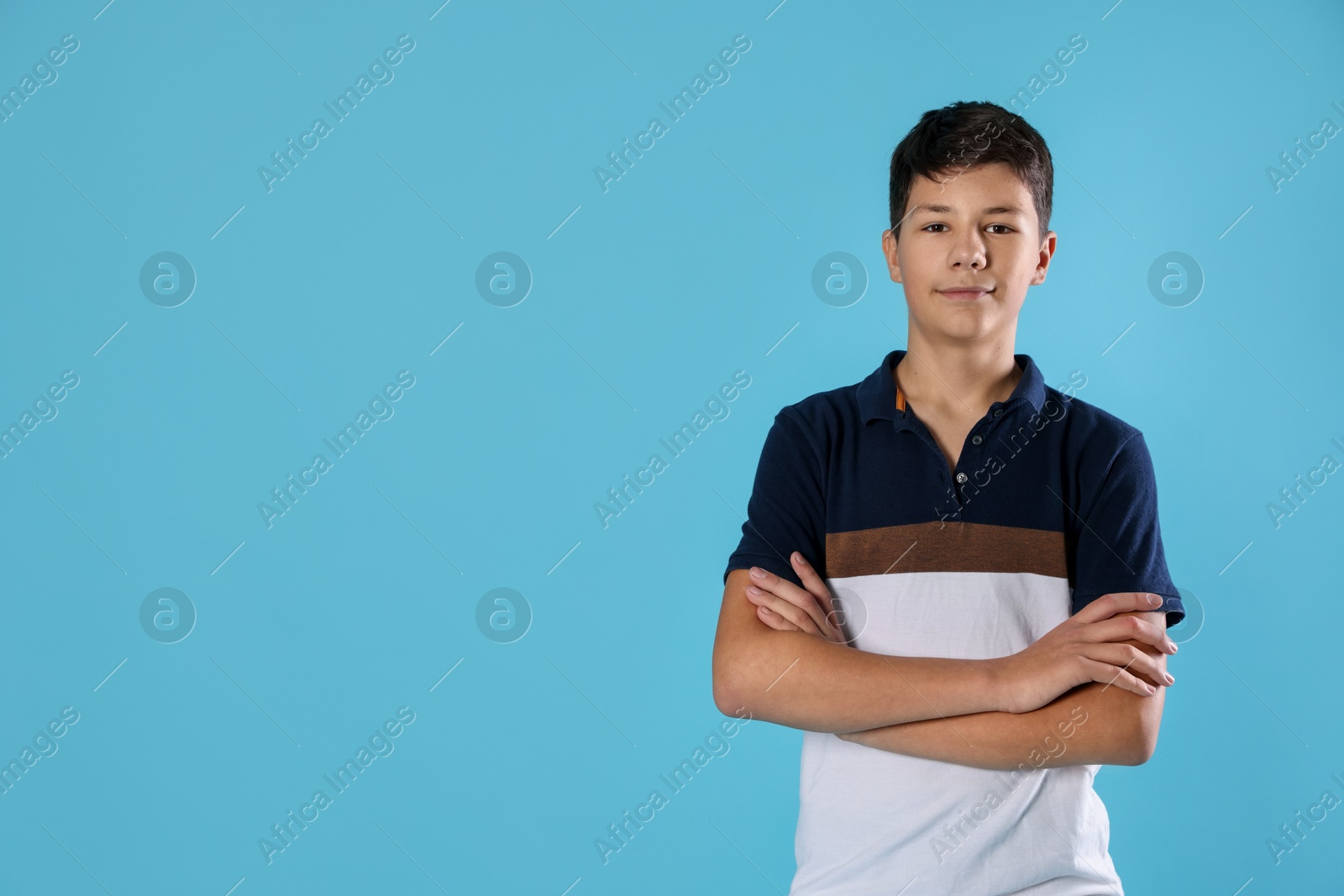 Photo of Portrait of teenage boy with crossed arms on light blue background, space for text