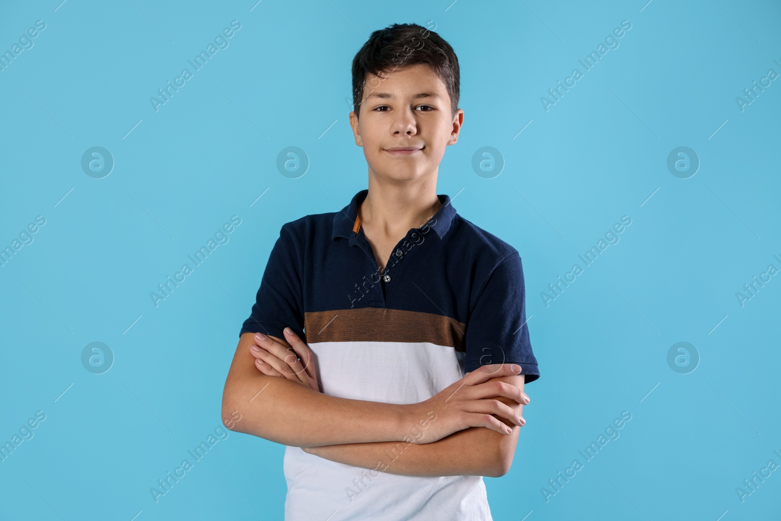 Photo of Portrait of teenage boy with crossed arms on light blue background