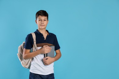 Photo of Portrait of teenage boy with books and backpack on light blue background, space for text