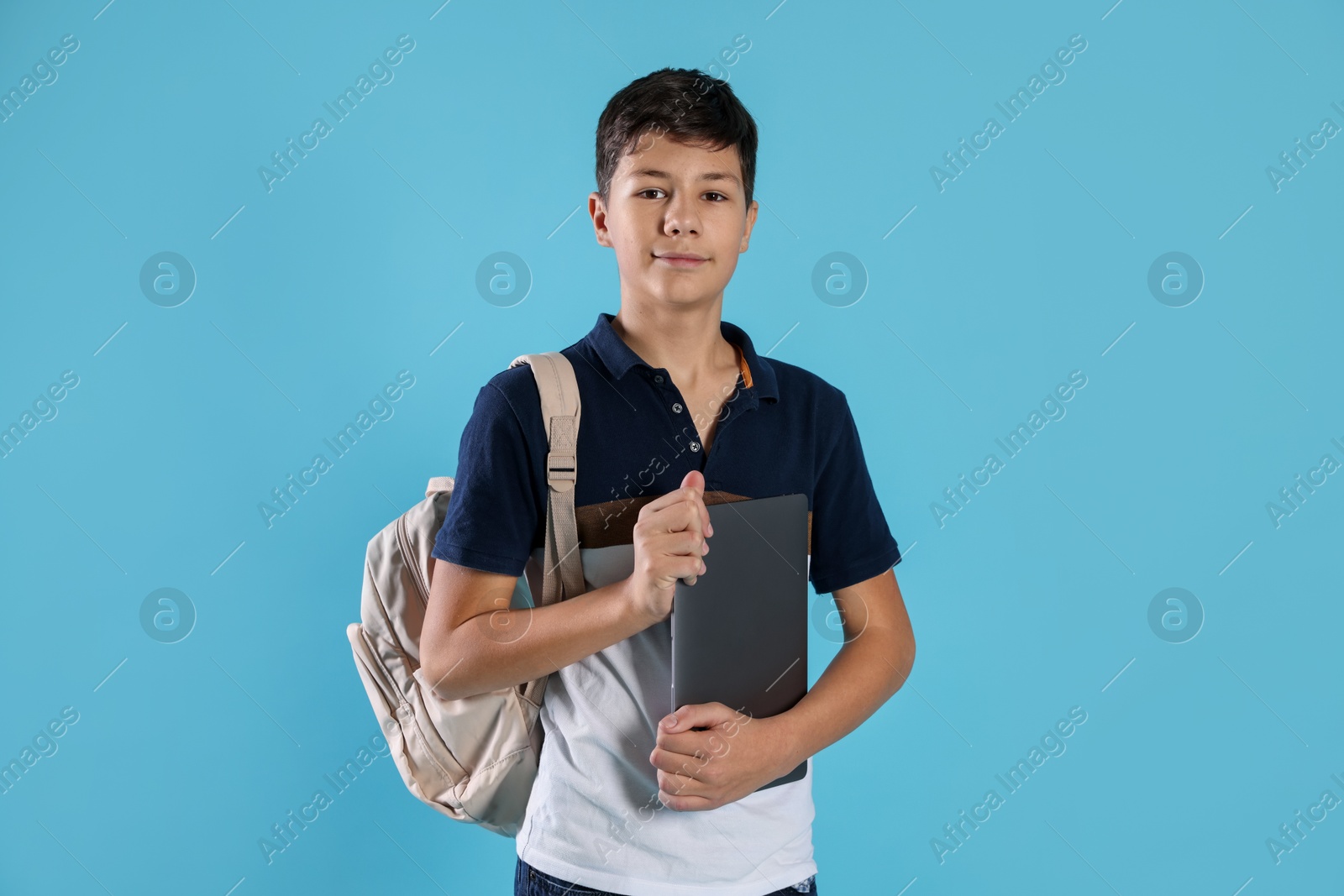 Photo of Portrait of teenage boy with laptop and backpack on light blue background