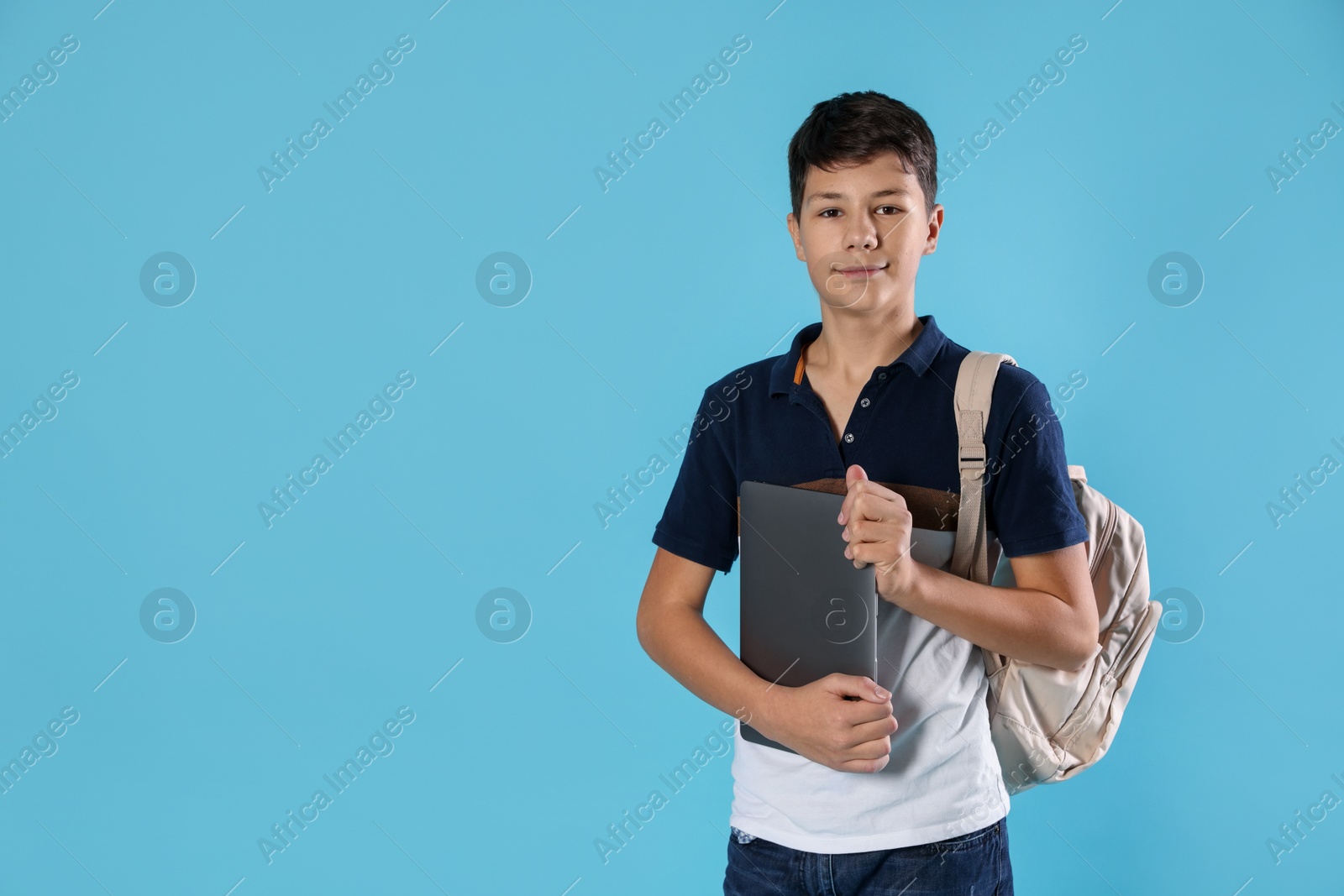 Photo of Portrait of teenage boy with laptop and backpack on light blue background, space for text