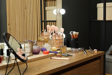 Photo of Makeup room. Wooden dressing table with mirrors and different beauty products indoors