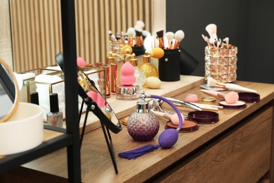 Photo of Makeup room. Mirror and different beauty products on wooden dressing table indoors