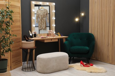 Photo of Makeup room. Wooden dressing table with mirror, different beauty products, shoes and pouf indoors